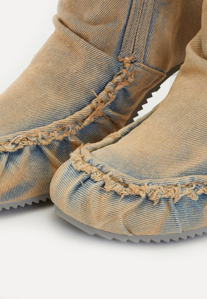 Denim-Ankle-Boots mit fransigen Kanten, in hellblau und beige, aus strukturiertem Stoff und mit einer gezackten Gummisohle. Gestickte Details rund um die Oberkante.