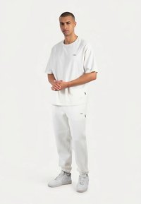 Vit bomulls-t-shirt med korta ärmar och en minimalistisk logotyp, kombinerad med vita mjukisbyxor. Bärs med vita sneakers. Enkel, avslappnad passform.