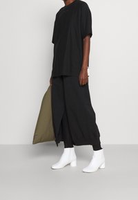 Svart oversized t-shirt, svarta byxor med framslits, vita ankelboots och en olivgrön väska. Enkelt design med kontrasterande färger.