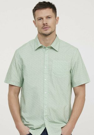 Chemise à manches courtes en tissu vert clair avec un motif floral subtil. Elle possède une poche poitrine unique et un col classique.