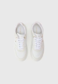 Bijela tenisica s perforiranim dizajnom, kontrastnim bež detaljima i bijelim vezicama. Ima zlatni logo sa strane i mekan, gladak materijal.