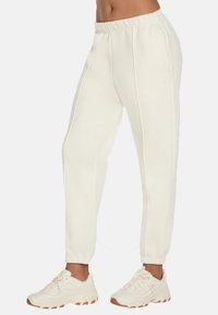 Witte sweatpants met een elastische tailleband en boorden, voorzien van zijzakken en een logodetail aan de voorkant links. Gekleed met beige sneakers.