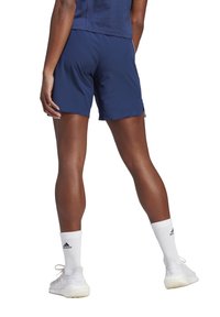 Marineblauwe sportshorts met een gladde afwerking en een relaxte pasvorm, gecombineerd met witte kniekousen en witte sportschoenen.
