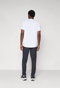 Mandig atletisk outfit bestående af en kortærmet hvid skjorte og mørkegrå bukser med en glat tekstur og tætsiddende design. Sorte sneakers.