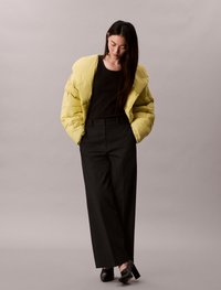 Φουσκωτό κίτρινο μπουφάν με λεία υφή, μαύρη μπλούζα, ψηλόμεσα μαύρα παντελόνια και μαύρες γόβες. Απλός σχεδιασμός, χωρίς σχέδια ή διακοσμητικά στοιχεία.