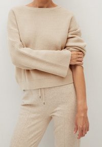 Béžový žebrovaný svetr s širokými rukávy a lodním výstřihem. Materiál má jemnou strukturu. V kombinaci s odpovídajícími béžovými kalhotami na šňůrku.