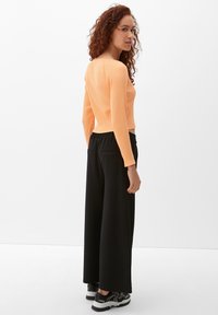 Geribbelde oranje lange mouw top in combinatie met zwarte broek met wijde pijpen. De top is cropped en de broek heeft een ontspannen pasvorm met zakken.
