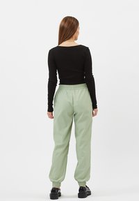 Zwarte lange mouwen top gecombineerd met lichtgroene elastische broek en zwarte chunky plateau schoenen, vastgelegd vanuit de achterkant.