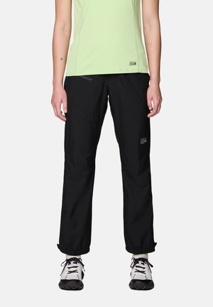 Person trägt schwarze Outdoorhose und weiße Wanderschuhe, steht mit entspannt an den Seiten hängenden Armen.