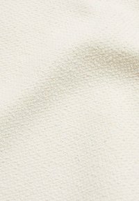 Tissu blanc texturé avec un motif tissé, présentant une surface douce et légèrement en relief. Le matériau semble léger et respirant.