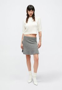 Grå strikket nederdel kombineret med en hvid cropped sweater med korte ærmer. Outfittet fuldendes med hvide ankelsokker og spidse sko.