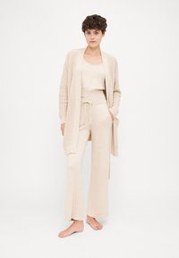 Beige knit cardigan with open front and pockets, layered over a matching fitted tank top and drawstring pants, showcasing a relaxed fit.