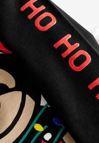 Schwarzer Stoff mit leuchtend rotem "HO HO HO"-Text, versehen mit einem beigen Design und Feiertagslichtern. Glatte Textur und lebendige Farben insgesamt.