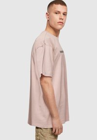 Overdimensioneret lyserød bomulds T-shirt med korte ærmer og rund hals; har sort tekst på fronten. Glat stofstruktur.