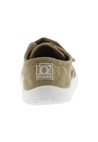Zapato slip-on de lona color caqui con suela de goma blanca, que presenta una pequeña etiqueta de logo en la parte trasera. Textura suave y forma redondeada.