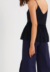 Svart peplumtopp med V-ringning och tunna axelband, tillverkad av mjukt tyg, med en skräddad midja och genomskinlig nederkant.