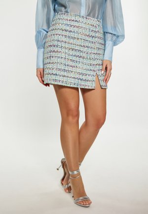 Lichtblauwe tweed mini-jurk met een gestructureerde afwerking en een veelkleurenpatroon, voorzien van een zijsplit. Gecombineerd met zilveren sandalen met bandjes.