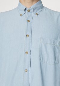 Jasnoniebieska koszula zapinana na guziki z mieszanki bawełny, z kołnierzykiem, siedmioma guzikami i jedną kieszonką na piersi. Miękka tekstura z luźnym krojem.