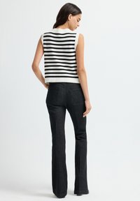 Schwarz-weißer gestreifter ärmelloser Top mit einem gekürzten Design, kombiniert mit hoch taillierten schwarzen Jeans mit geradem Bein und Hintertaschen.