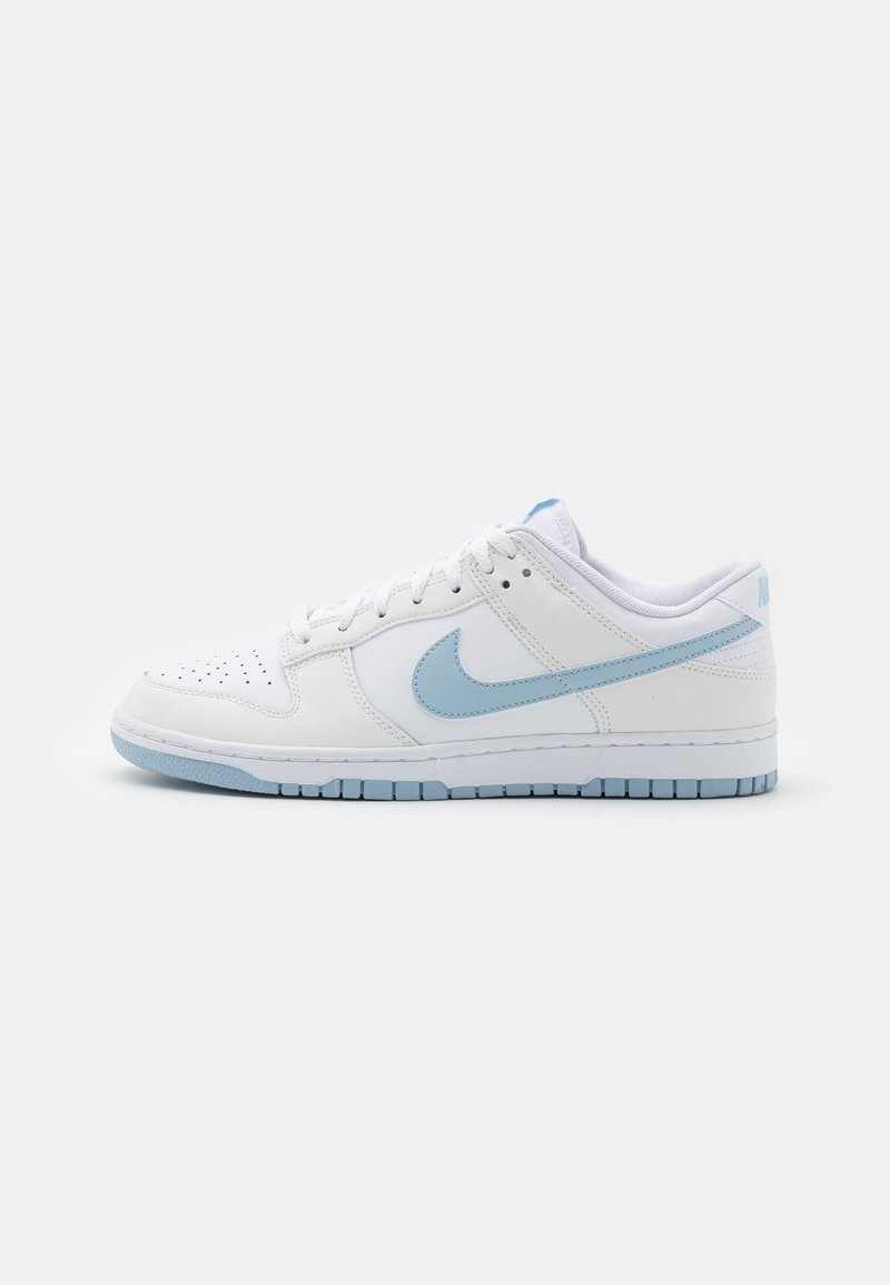 Sapatilha baixa branca com o símbolo Nike em azul claro, detalhes em azul claro na sola e atacadores brancos, sobre um fundo neutro e simples.