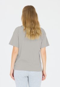 Grå kortärmad t-shirt sedd bakifrån, med en avslappnad passform och mjuk bomullskvalitet, parat med ljusgråa sweatpants.