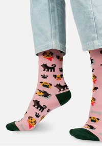 Różowe skarpetki z kolorowymi motywami psa, w tym różnymi rasami i odciskami łap, z ciemnozielonym palcem i mankietem. Wykonane z mieszanki bawełny.