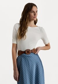Vit kortärmad topp i kombination med en blå prickig kjol. Outfiten har ett brunt bälte med spänne och en strukturerad yta.