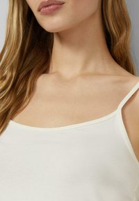 Biały top na ramiączkach, z cienkimi paskami, okrągłym dekoltem, wykonany z miękkiej bawełny o gładkiej fakturze, zapewniający komfort i dopasowanie.