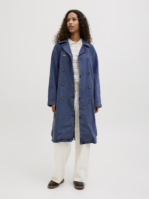 Denim trench coat med dobbelspent design, store knapper, sidelommer og en avslappet passform. Båret over en stripete skjorte og brede bukser.