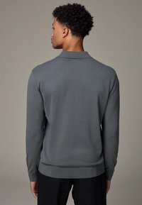 Grauer Pullover mit langen Ärmeln und Kragen. Besitzt eine glatte Textur und gerippte Bündchen sowie einen Saum. Minimalistisches Design ohne sichtbare Muster.