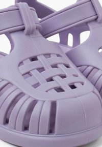 Purple plastic sandals with a woven design, featuring cut-out details and a textured surface. Adjustable strap for secure fit.