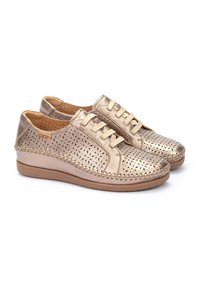 Zapatos de cuero perforado metálico dorado con punta redonda, diseño de cordones, suela en contraste color marrón claro y costuras decorativas en los bordes.