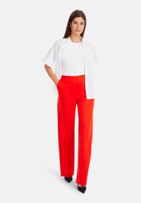 Weißes, übergroßes Button-Up-Hemd über einem figurbetonten weißen strukturierten Top und leuchtend roten hochtaillierten, weiten Hosen, kombiniert mit schwarzen High Heels.