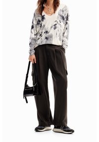 Blusa a V con stampa floreale e di giornale in bianco e nero, abbinata a pantaloni cargo neri larghi, borsa a tracolla nera e sneakers nere.