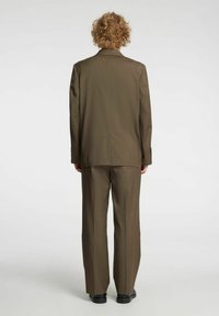 Brązowy garnitur na miarę, z marynarką z klapą z wycięciem i dopasowanymi spodniami, wykonany z teksturowanej tkaniny, z prostymi nogawkami i minimalistycznymi detalami.