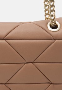 Beige quiltet læderhåndtaske sektion med diamantstikninger, guldkædetråd gennem poleret guldøje.