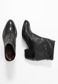 Botas de cuero negras hasta el tobillo con puntera redondeada, detalles de costura sutil y un tacón bajo y apilado. Cierre de cremallera en el lateral.