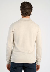Beige stickad tröja med polo-krage, långa ärmar och ribbade mudd och nederkant. Slät textur, figurnära siluett, minimala detaljer.