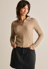 Beige strukturerad långärmad överdel med krage och knapprad, matchad med en svart jeanskjol med fickor och fransad nederkant.