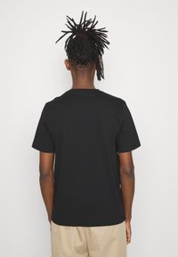 Svart bomullströja med rund hals och korta ärmar. Har en enkel design och rak passform, sedd bakifrån.