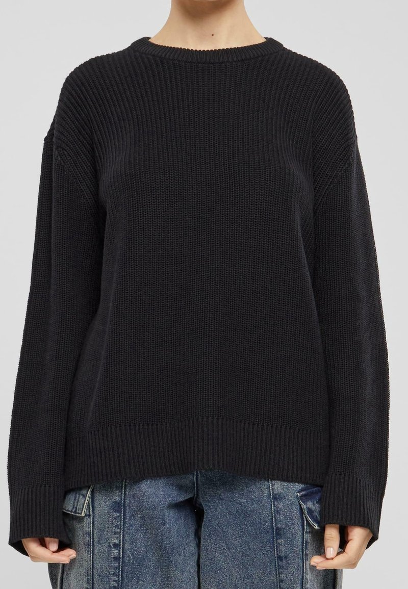 Osoba nosząca czarny sweter z prążkowanego materiału z długimi rękawami, zestawiony z luźnymi, niebieskimi dżinsami.