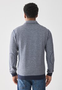 Navy blue, textured sweatshirt with a high collar, ribbed cuffs, and elbow patches; made from soft, knitted material. Casual design.