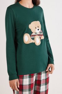 Camisa verde de manga larga con un aplique de oso de peluche en un suéter con patrón. Combinada con pantalones de pijama de cuadros rojos y blancos.