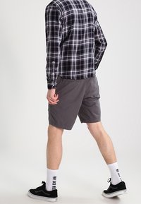 Szare szorty wykonane z lekkiego materiału, zestawione z czarno-białą koszulą w kratę. Noszone z czarnymi sneakersami i białymi skarpetkami do kostek.