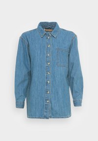 Lys blå denimskjorte med knappestøtte i front, spiss krage og lange ermer. Har en enkelt brystlomme og gullhardware.