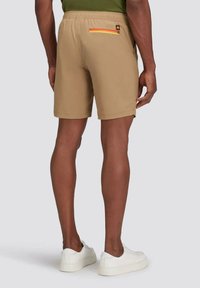 Shorts beige con una vita elasticizzata, dotati di una tasca posteriore con zip e un accento multicolore, abbinati a sneakers bianche.