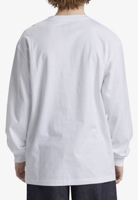Long-sleeve white t-shirt with a round neckline, featuring a loose fit and soft cotton fabric, visible stitching, and ribbed cuffs.