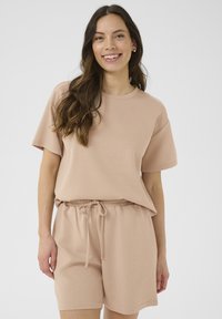 Kortärmad t-shirt med rund halsringning och matchande shorts i ljusbeige tyg med elastisk midja och dragsko. Mjuk textur och avspänd passform.