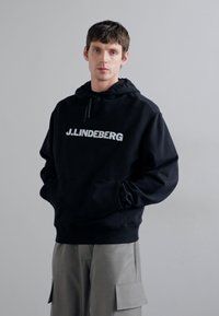 Felpa con cappuccio nera realizzata in tessuto morbido, con un logo bianco "J.LINDEBERG" sul petto, dal fit rilassato e tasca a marsupio.