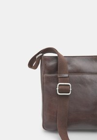 Borsa a spalla in pelle marrone con superficie texture, tracolla in tessuto regolabile e dettaglio in fibbia color argento. Design minimalista.